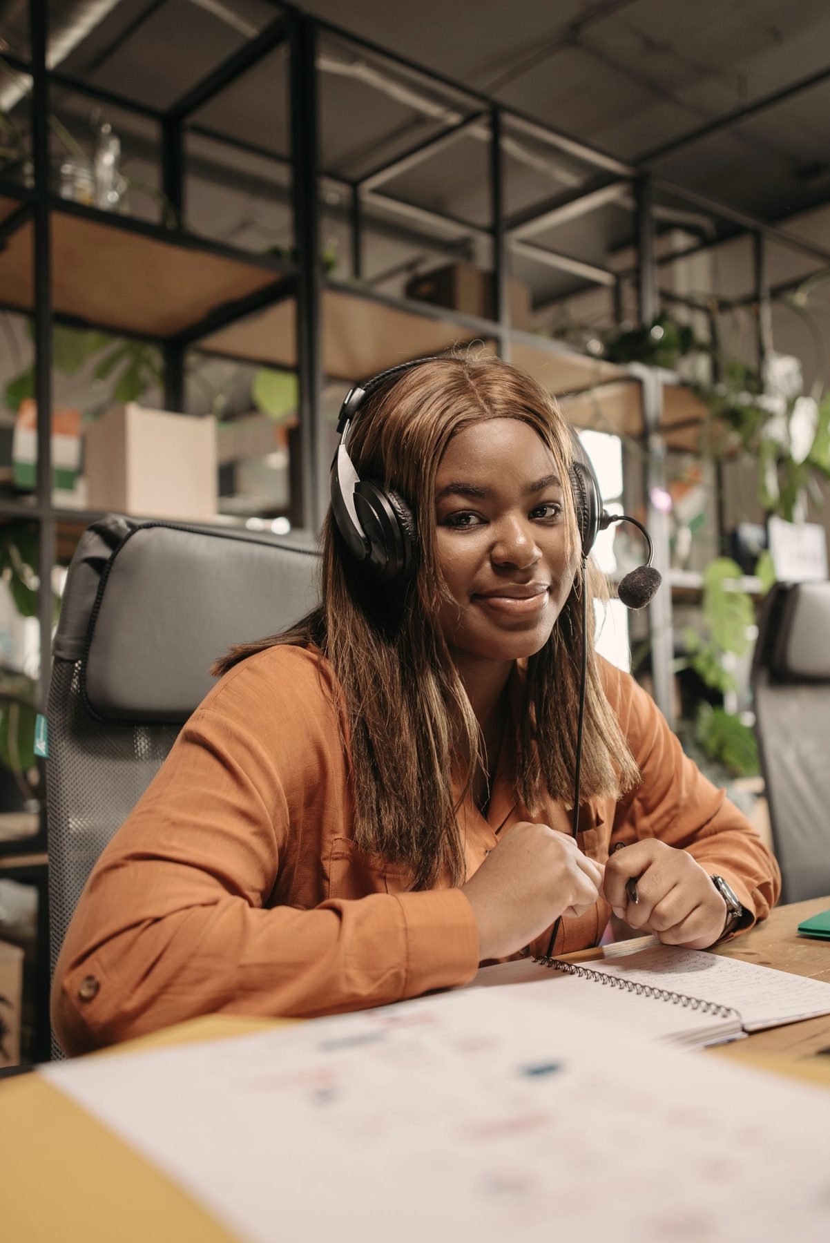 An operator in an orange sweater at her desk with a headset