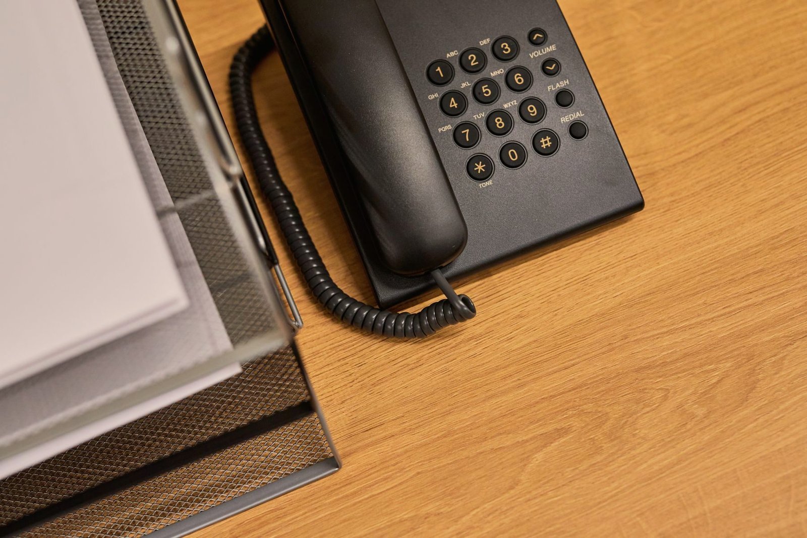 A desk telephone and documents on a wooden office desk